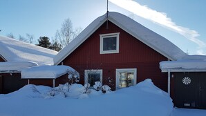 Um celeiro vermelho com duas janelas e uma porta, rodeado por neve.