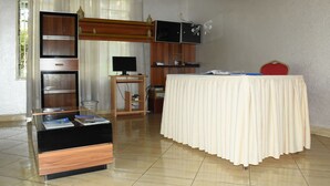 A room with a wooden cabinet, a television, a table with a white tablecloth, and a red chair. - Tinho Guest House (Kigali)