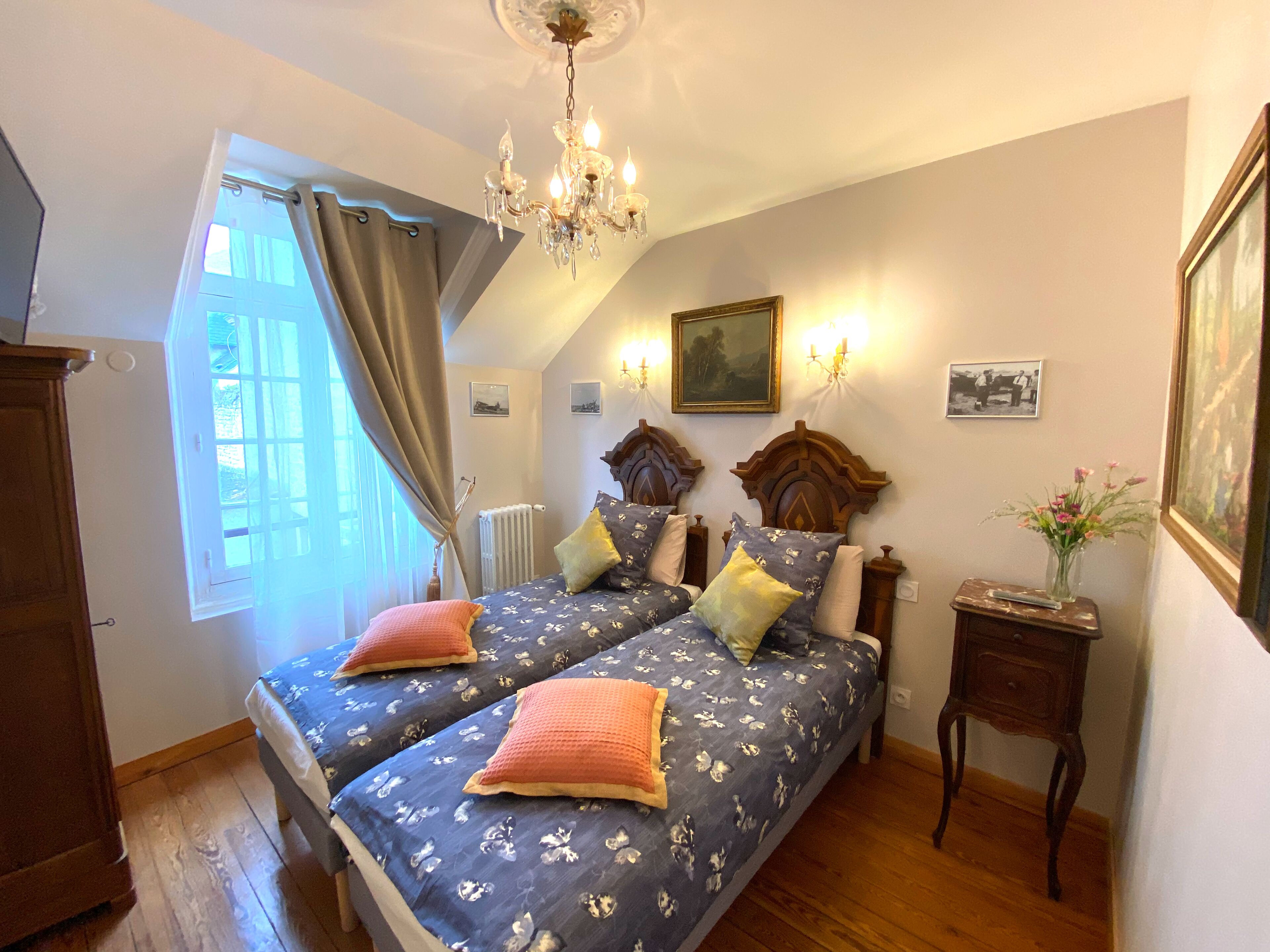 A bedroom with two beds, a chandelier, a radiator, and a small table with a vase.