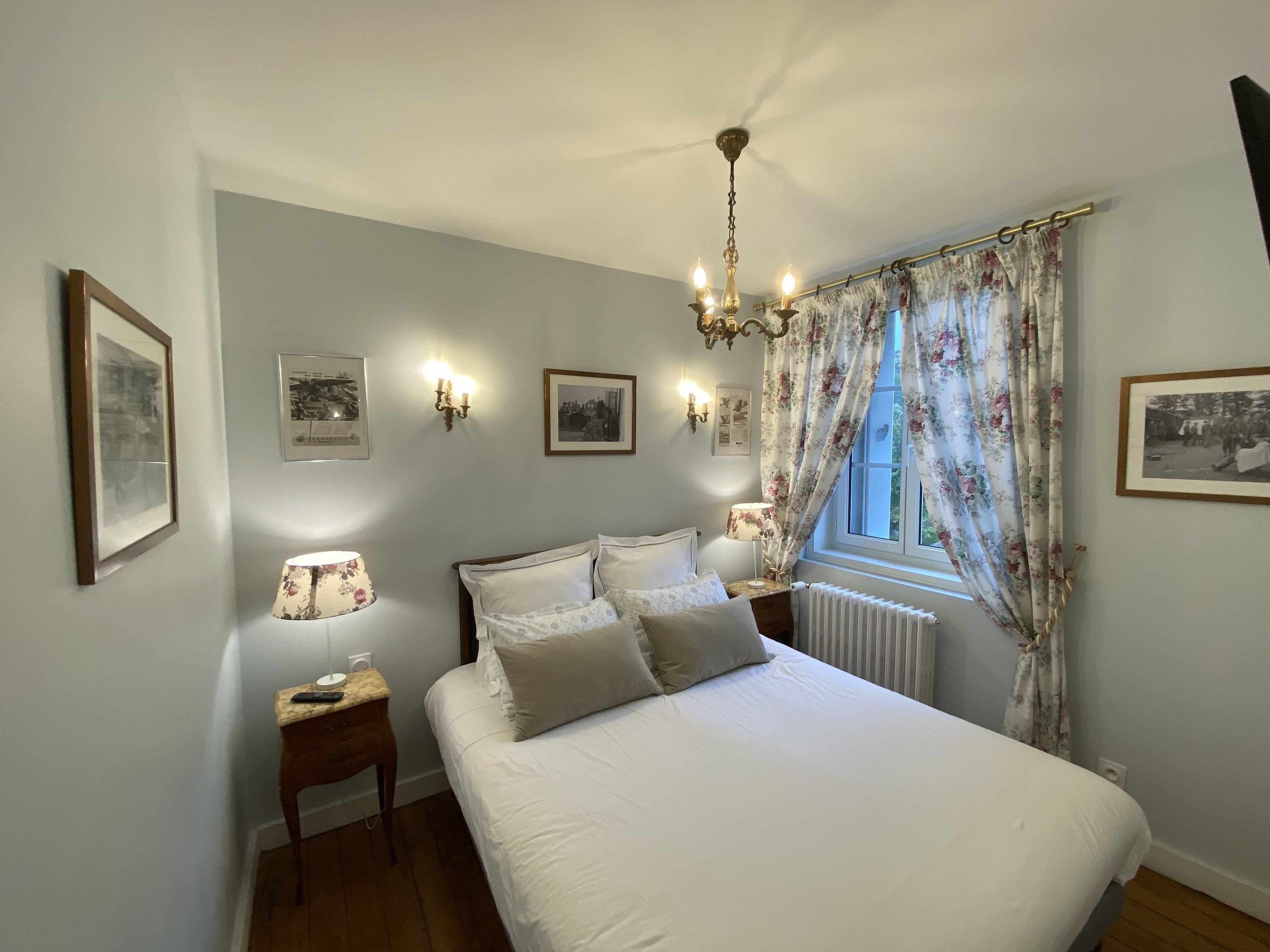 Une chambre à coucher avec un grand lit, des lampes de chevet, un lustre et des rideaux à motifs floraux.