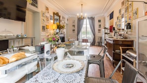 Un espace repas avec une table en verre, des chaises et un buffet garni de pâtisseries.