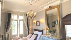 Une chambre à coucher luxueuse, dotée d’un grand lit, d’un lustre, d’une cheminée et d’un grand miroir.