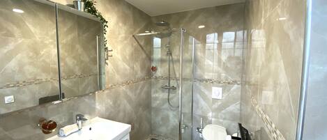 A modern bathroom with a glass-enclosed shower, a white sink, and a toilet.