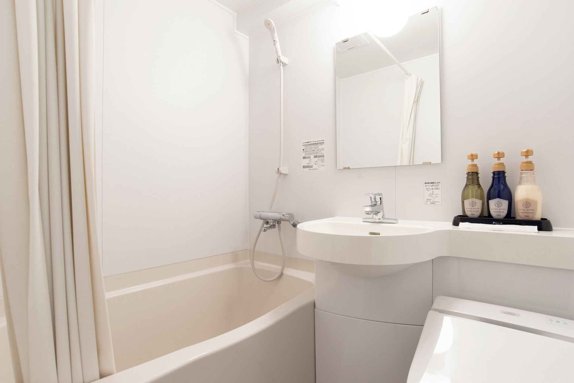 A bathroom with a bathtub, a sink, and a toilet. There are two bottles of shampoo and conditioner on the sink.