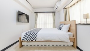 A modern bedroom with a bed, a flat-screen TV, and a ceiling light. - G-stays Shinjuku (Tokyo)