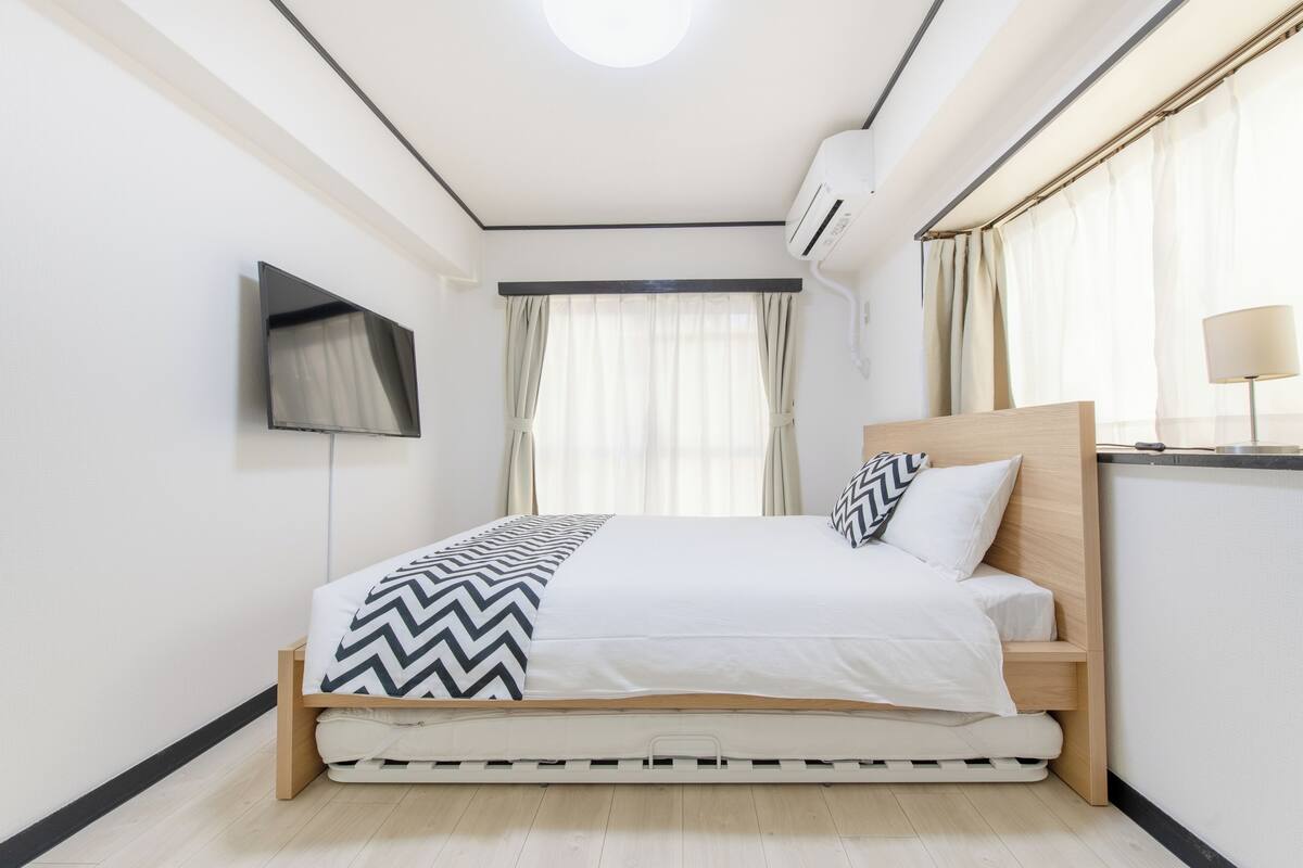 A modern bedroom with a bed, a flat-screen TV, and a ceiling light.