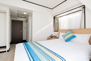 Een hotelkamer met een bed, nachtkastje, lamp, telefoon en een raam met gordijnen.