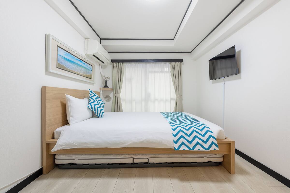 A neatly made bed with a wooden headboard, a wall-mounted TV, and a picture frame on the wall.