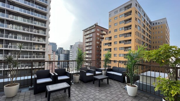 A rooftop terrace with outdoor seating, potted plants, and a cityscape view. - G-stays Shinjuku (Tokyo)