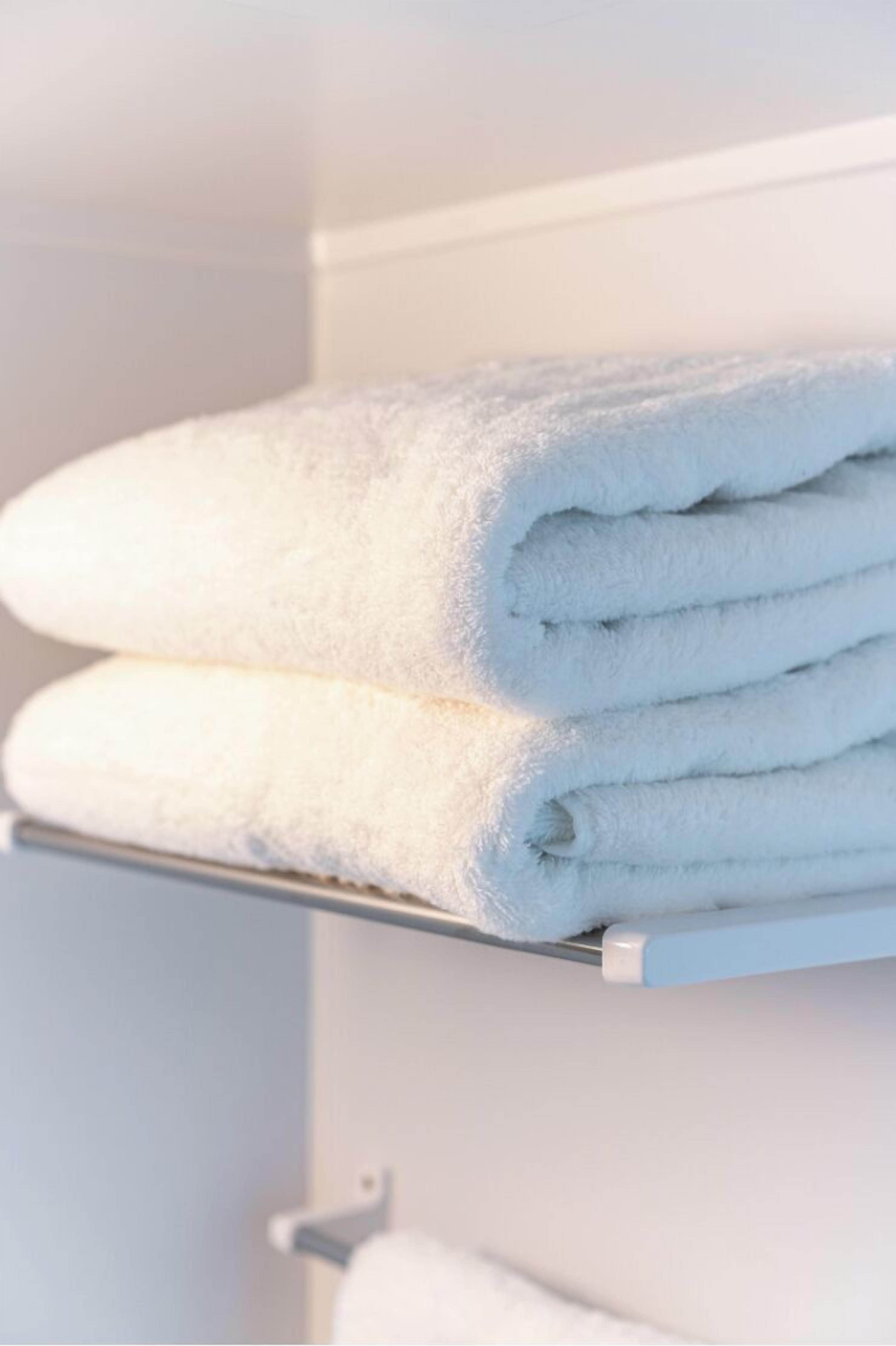 A stack of white towels on a metal shelf in a bathroom.