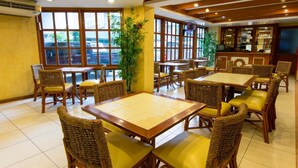 Um restaurante com mobiliário de vime, grandes janelas e chão de azulejos.
