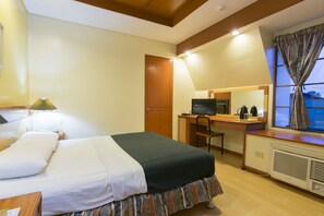 Una habitación de hotel con cama, escritorio, silla, televisión y ventana con cortinas.