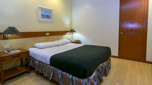 Quarto de hotel com uma cama, mesa de cabeceira, luminária, quadro na parede e porta de madeira.