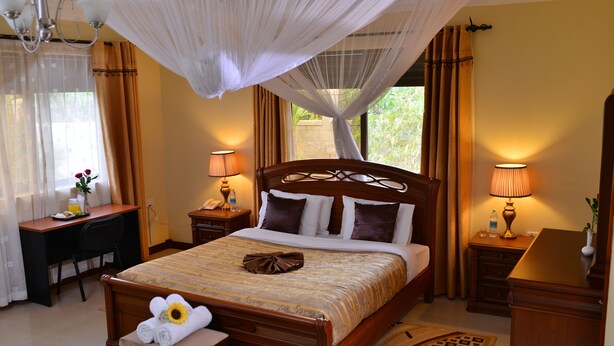A well-appointed hotel room with a large bed, bedside tables, a desk, and a chair. - Royal Victoria House (Kampala)