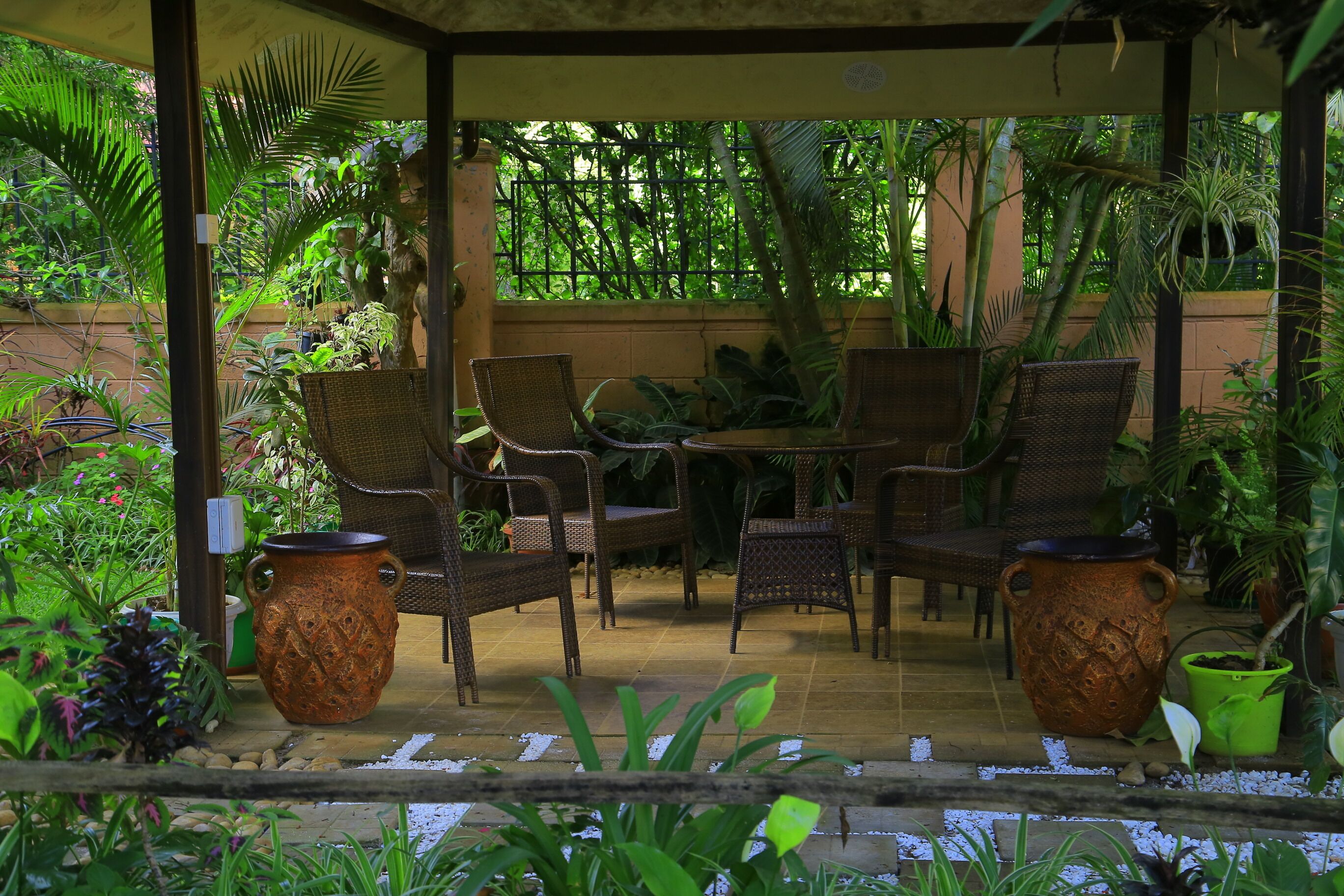 Un patio cubierto con mobiliario de mimbre, plantas en macetas y una gran maceta decorativa.