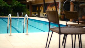 A swimming pool with metal ladders, a wicker chair, and a tiled patio area. - Royal Victoria House (Kampala)