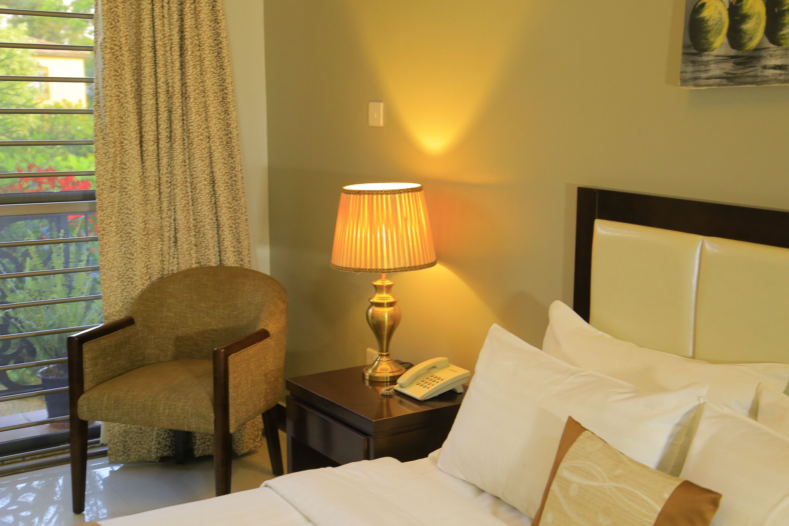 Ein Hotelzimmer mit einem Bett, einem Sessel, einem Nachttisch mit Lampe und einem Telefon.