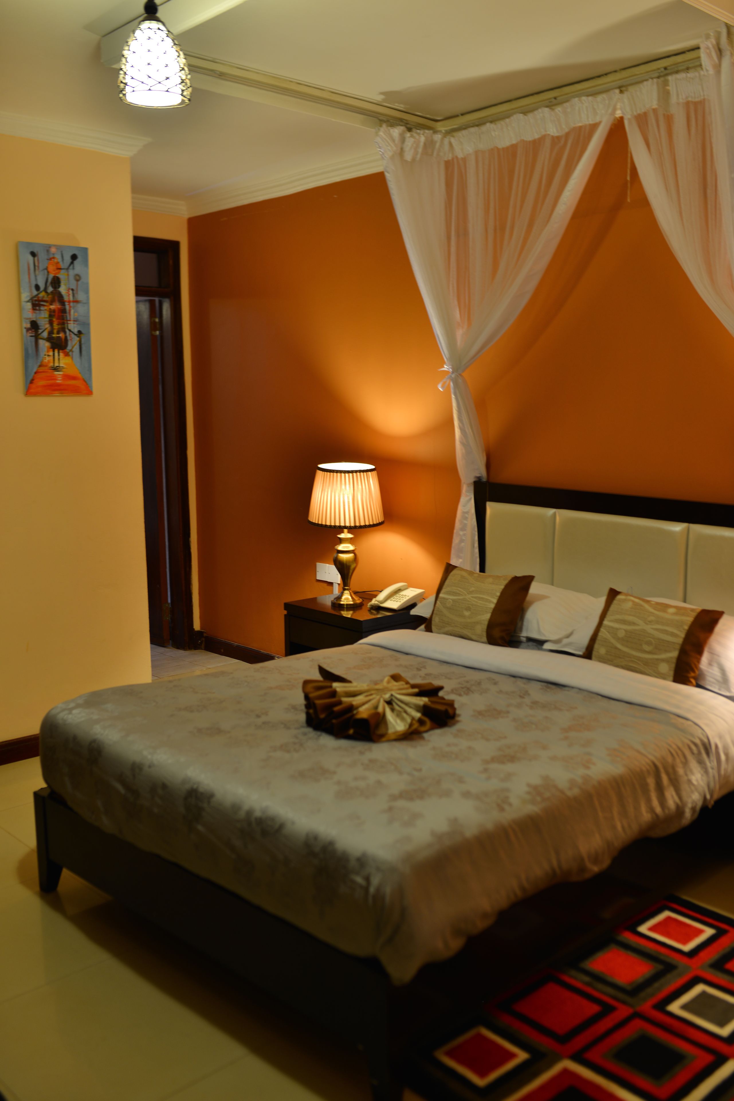 Una habitación de hotel con una cama, una mesita de noche, una lámpara y un cuadro en la pared.