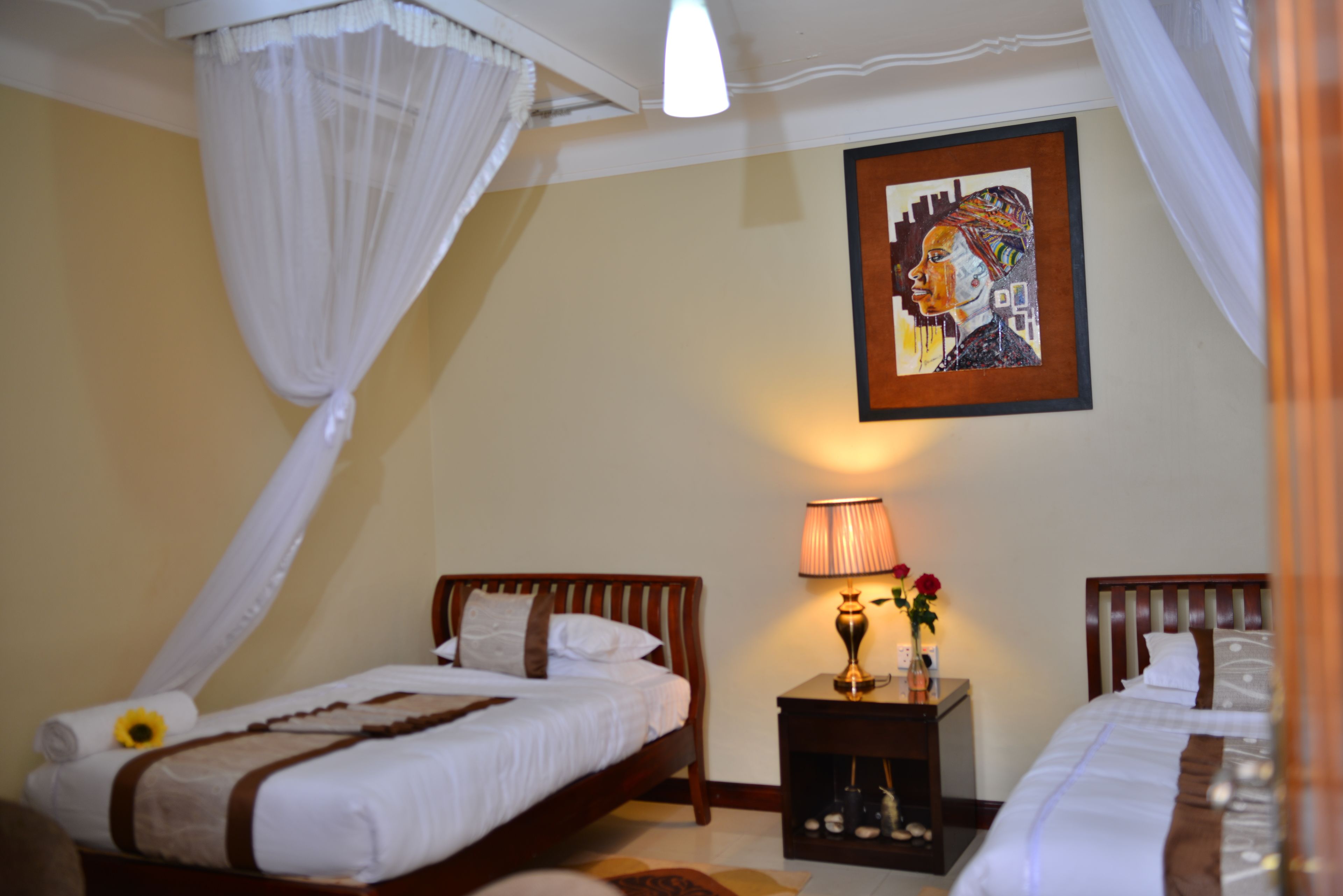 A bedroom with two beds, a nightstand with a lamp, and a framed artwork on the wall.