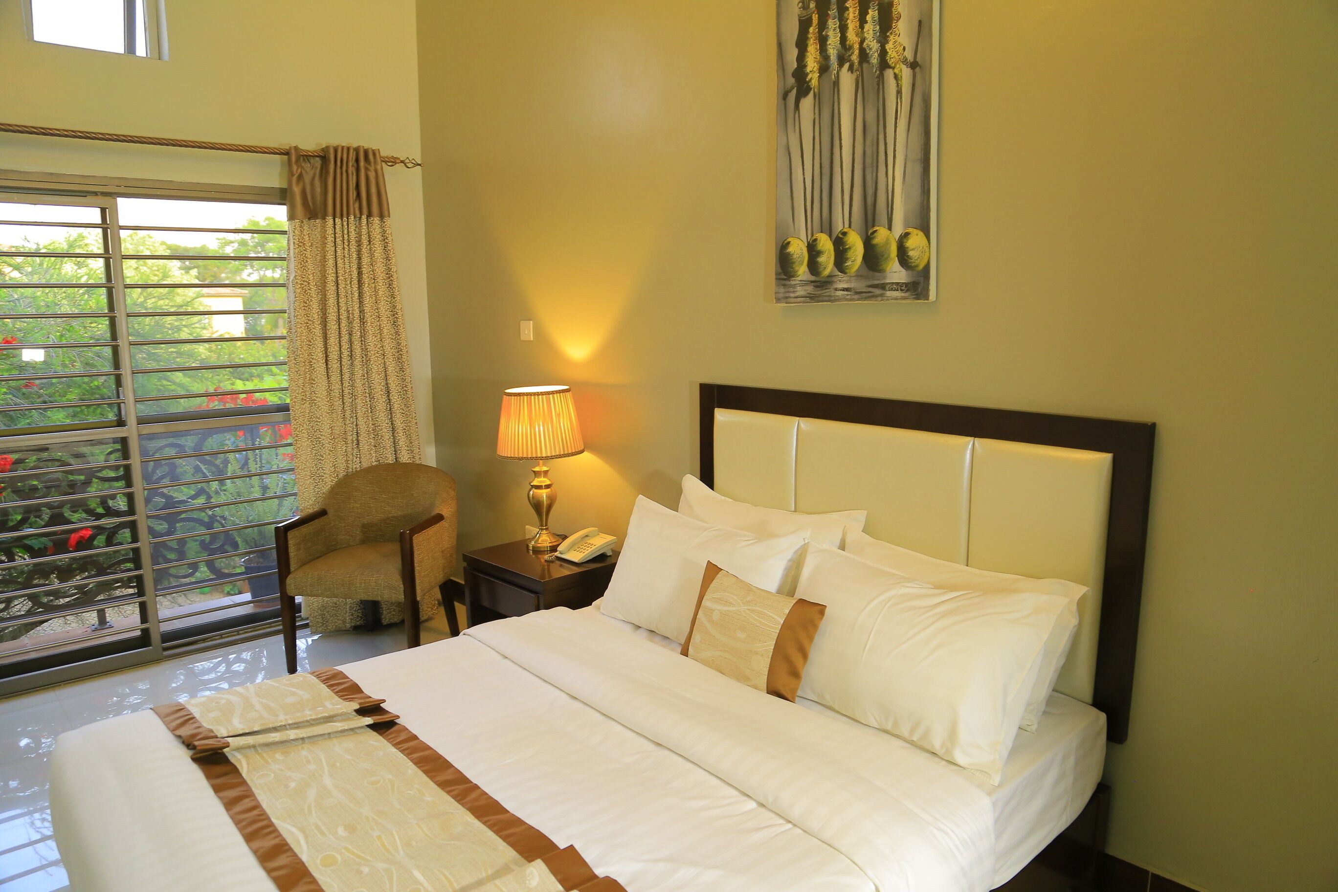 A hotel room with a bed, a chair, a nightstand, a lamp, and a painting on the wall.