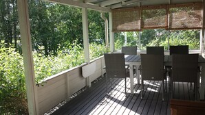 Ein überdachter Außenbereich zum Sitzen mit Tisch und Stühlen, umgeben von Pflanzen.