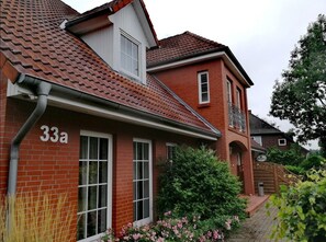 A red brick house with a tiled roof, a visible number '33a', and a small garden with pink flowers.