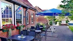 An outdoor seating area with tables and chairs, a blue umbrella, and a sign indicating a hotel. - Hotel & Gasthaus Zum Domkreuger (Walsrode)