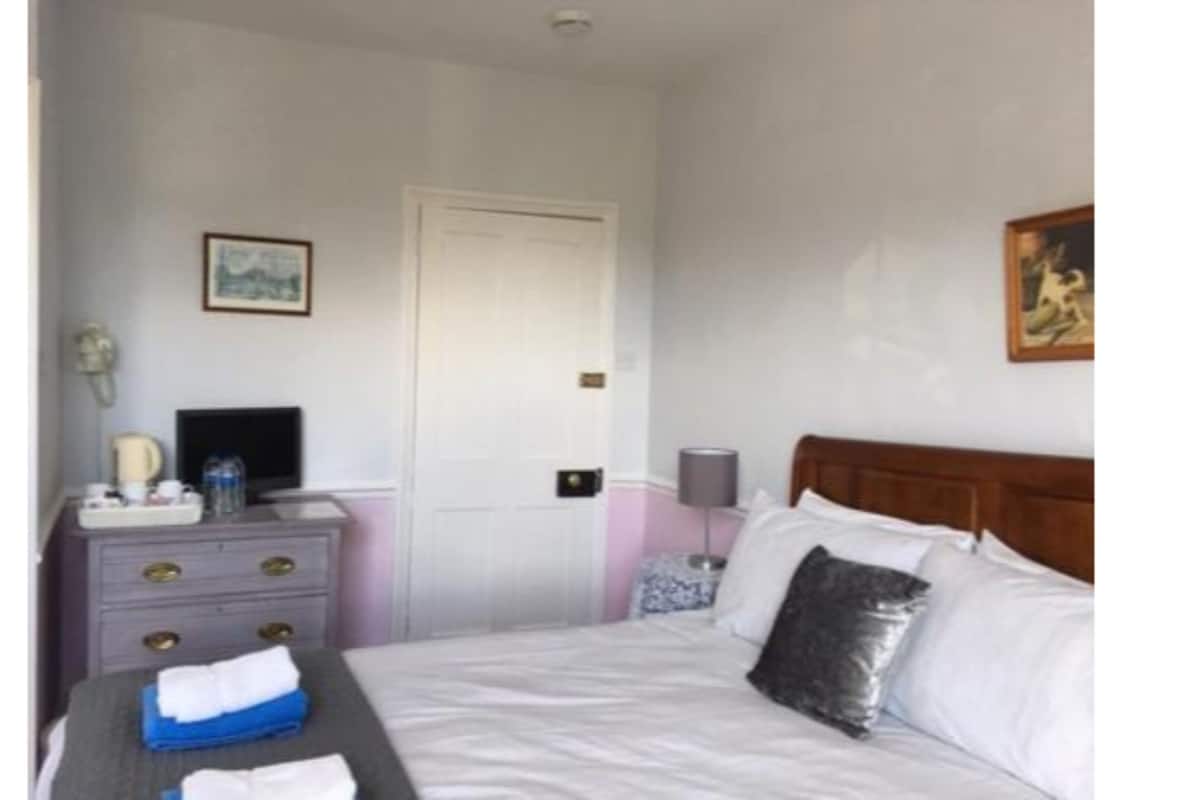 A hotel room with a bed, bedside table, dresser, and a door.