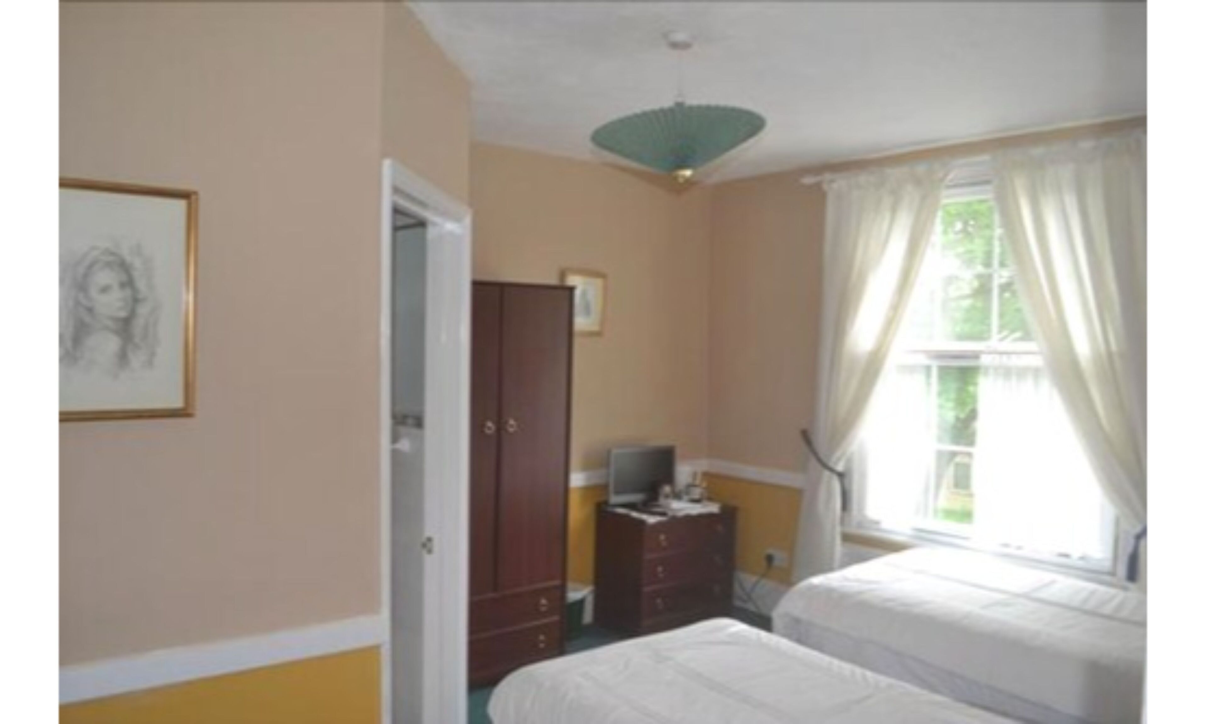 Un dormitorio con dos camas, un armario, un televisor sobre un tocador y una ventana con cortinas.