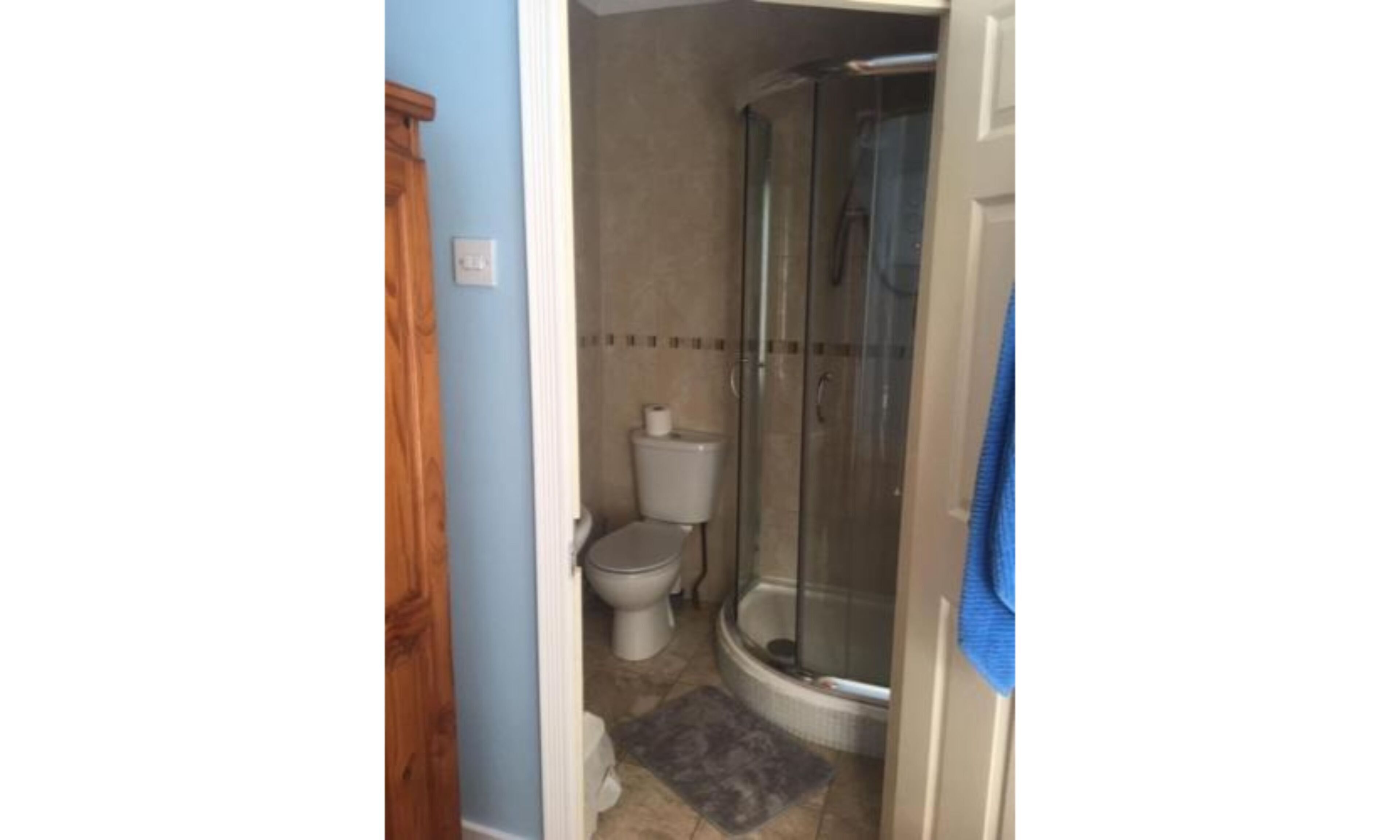 A bathroom with a toilet, a shower, and a blue towel hanging on the door.