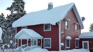 A red two-story house with a snow-covered roof and porch. - Villa Mia (Vidsel)