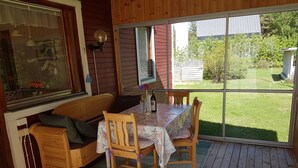 A cozy room with a wooden bench, a table with chairs, and a large window overlooking a garden. - Villa Mia (Vidsel)