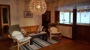 A cozy living room with a brown leather sofa, a wooden coffee table, and two armchairs. A large, intricate chandelier hangs from the ceiling, and a framed picture is displayed on the wall. - Villa Mia (Vidsel)