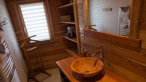 Bagno di una cabina di legno con lavandino in legno, uno specchio e una finestra con persiane.