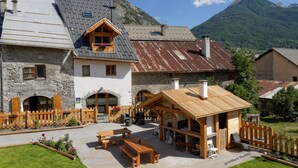 Un rifugio alpino rustico con pareti in pietra, panche di legno e una zona salotto esterna coperta.