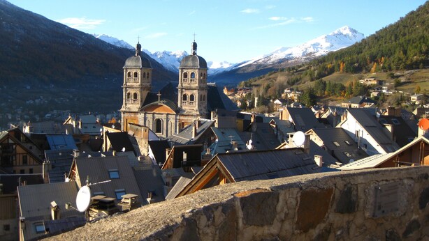 Una cittadina con una chiesa imponente caratterizzata da due campanili, circondata da edifici residenziali e montagne sullo sfondo.