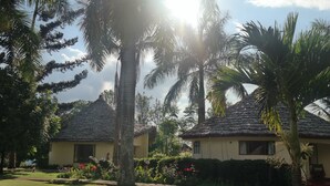 A tropical resort with thatched-roof cottages surrounded by lush greenery and flowering plants. - Kilemakyaro Mountain Lodge (Moshi)