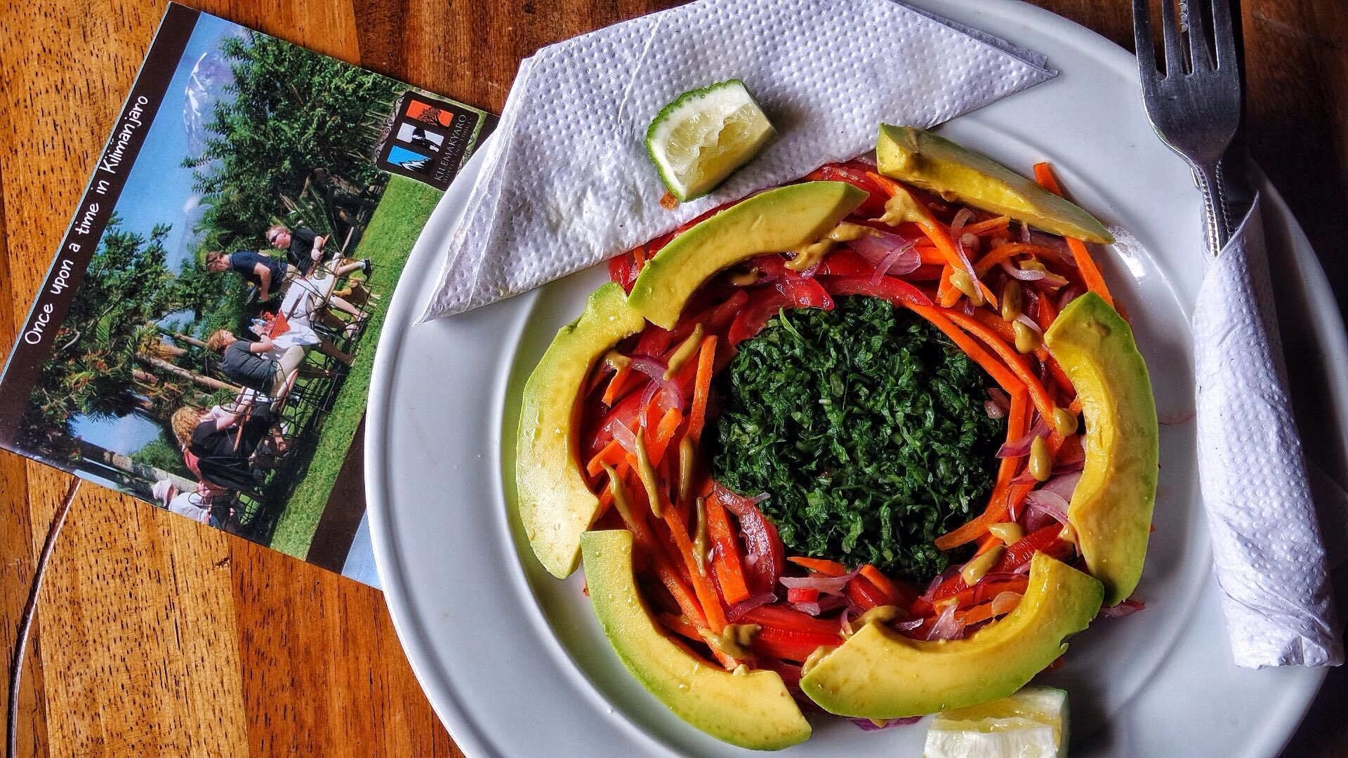 A plate of food with avocado, red peppers, and greens, a lime wedge, and a napkin on a wooden table.