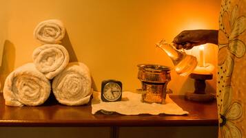 A wooden table with rolled towels, a clock, a candle, and a hand pouring water from a jug.