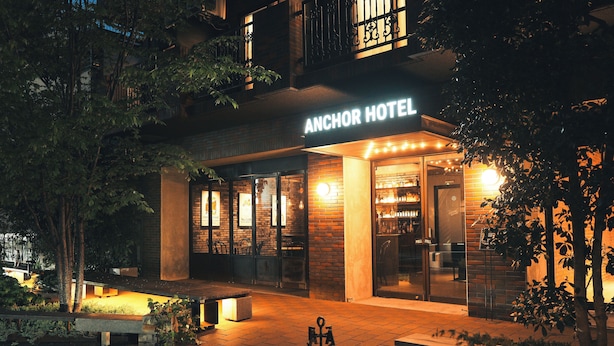 Exterior del Anchor Hotel con una entrada bien iluminada, zona de estar al aire libre y un cartel visible.