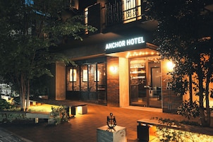 Exterior del Anchor Hotel con una entrada bien iluminada, zona de estar al aire libre y un cartel visible.