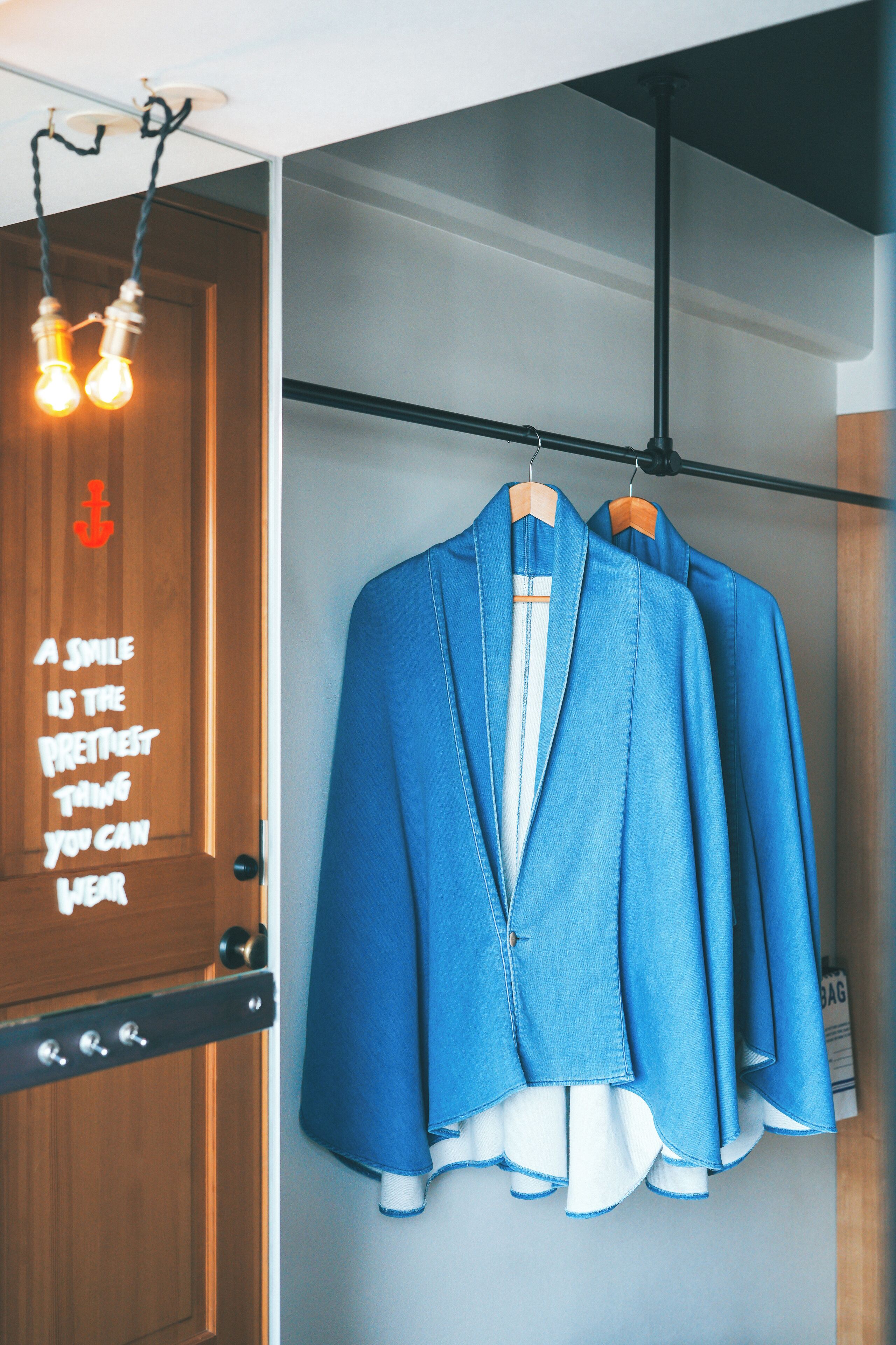 A wooden door with a motivational quote, a blue blazer hanging on a rack, and a light fixture above.