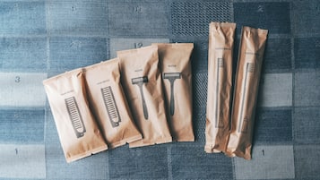 Five brown paper bags with different grooming tools labeled on them, placed on a checkered fabric surface.