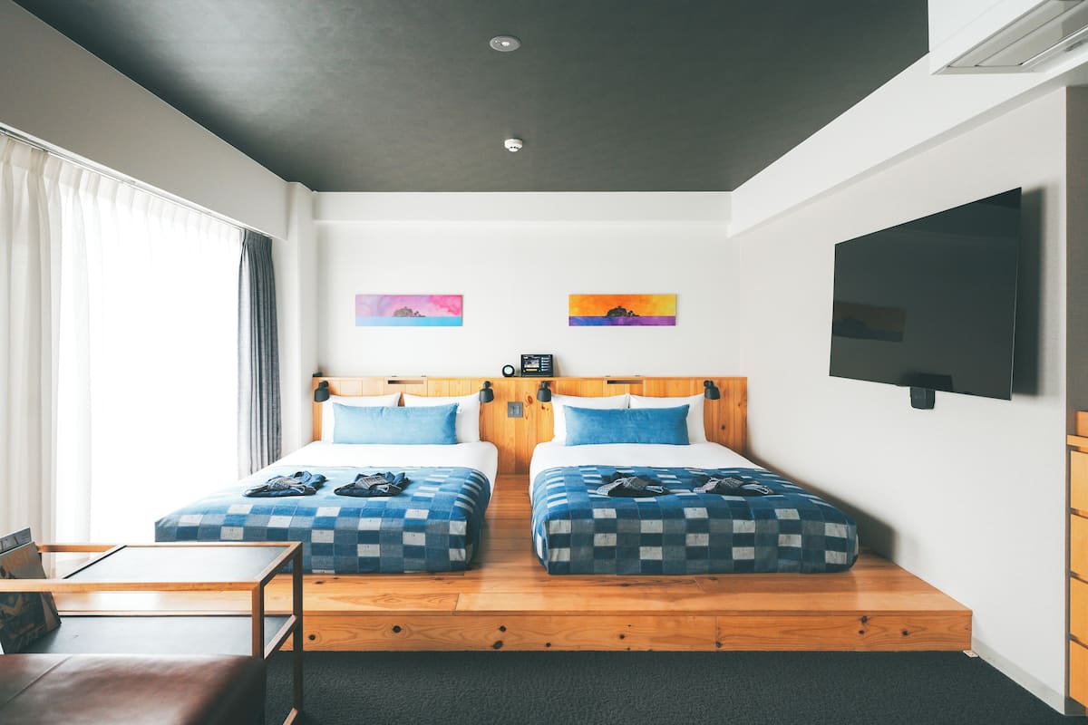 Une chambre d’hôtel avec deux lits, une télévision et des œuvres d’art accrochées aux murs.