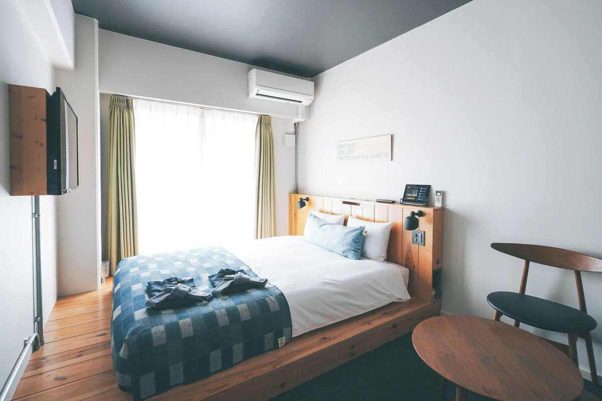 Une chambre d’hôtel avec un lit, une tête de lit en bois, une petite table et un téléviseur fixé au mur.