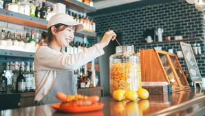 Un bar con estantes llenos de botellas de licores, un tarro de naranjas y limones en rodajas, y una vitrina de madera.