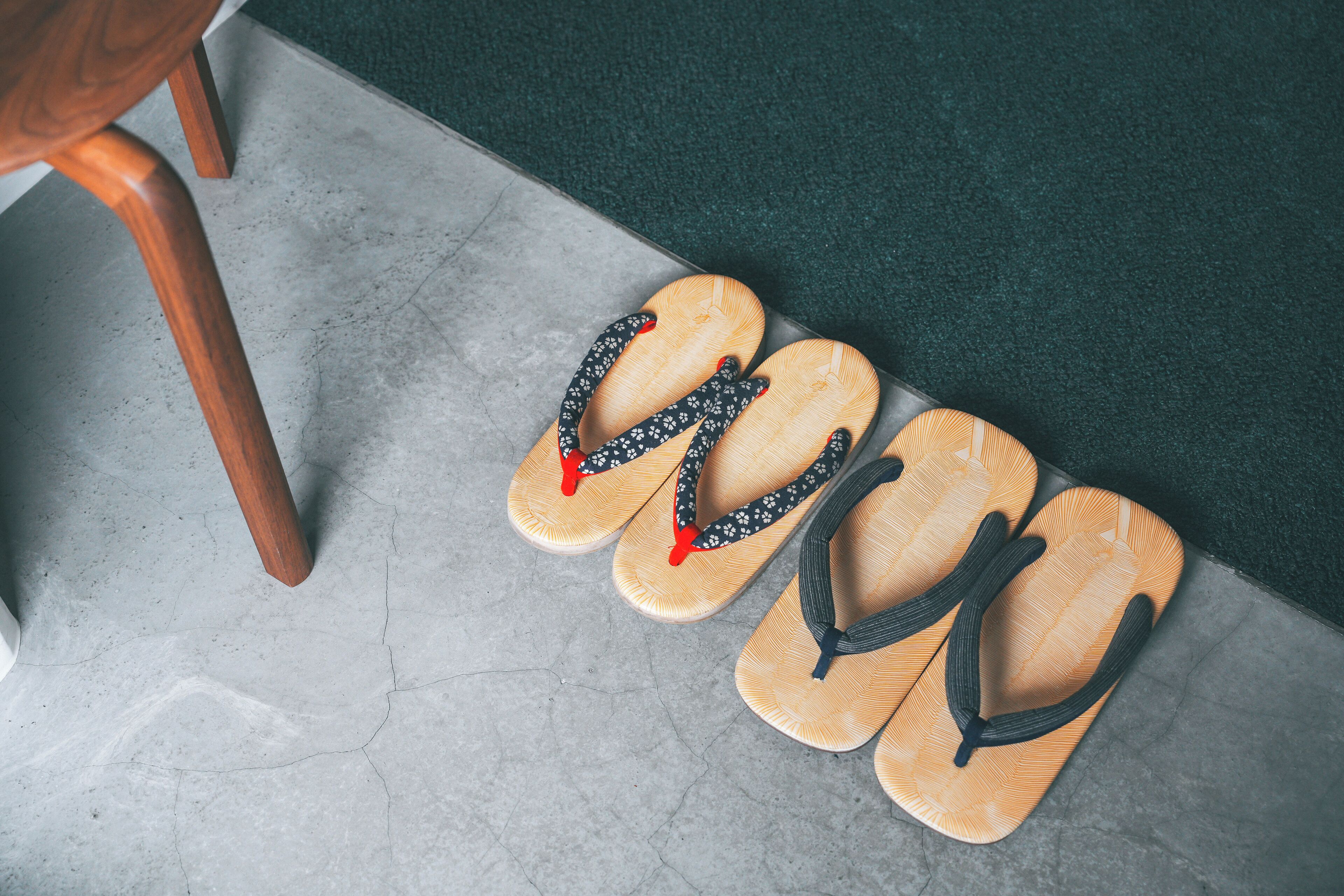 A pair of wooden flip-flops on a tiled floor next to a wooden chair.