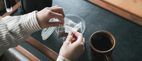 A person preparing a beverage with a kettle and a cup on a table.
