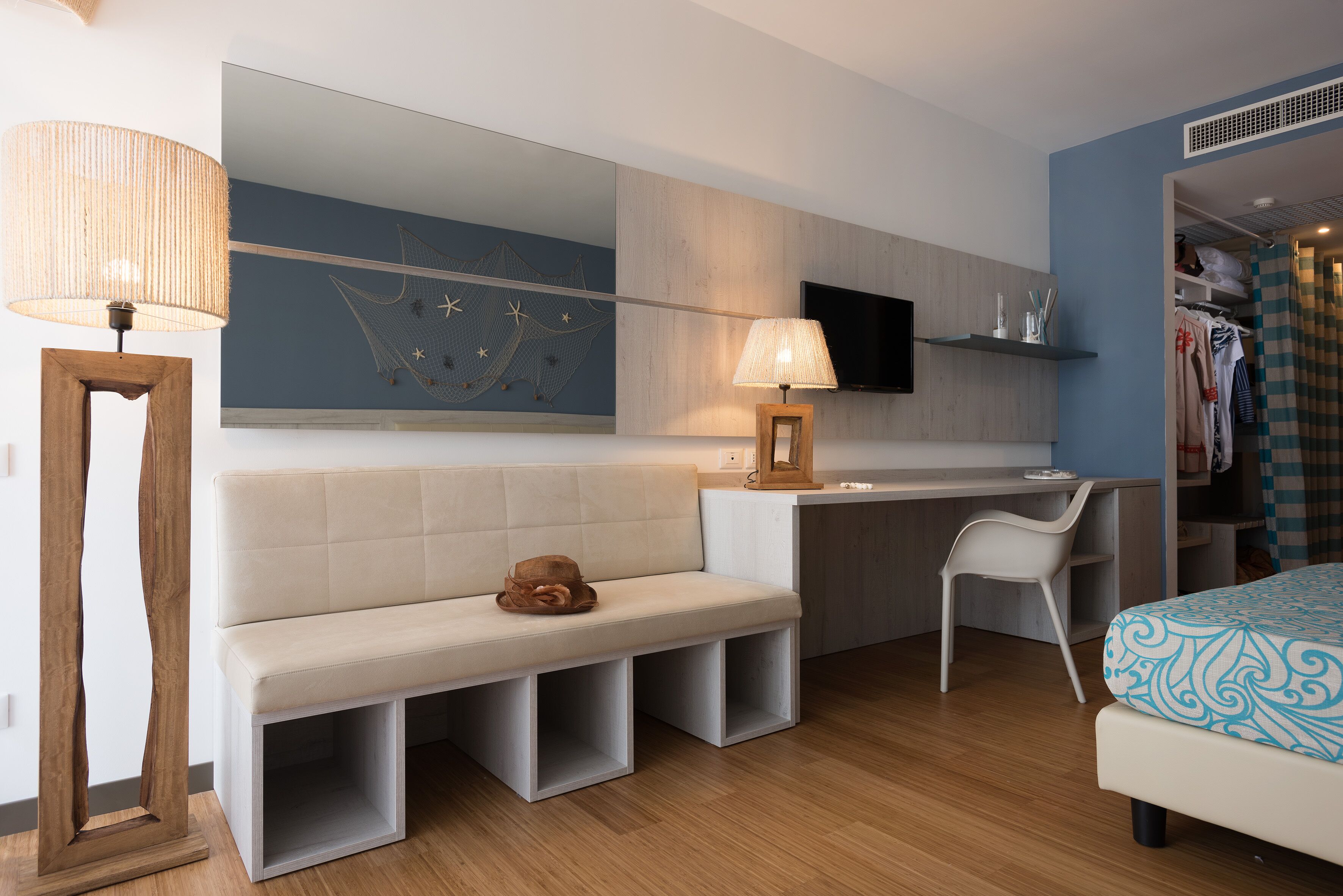 Ein modernes Hotelzimmer mit Sofa, Schreibtisch, Stuhl, Bett, großem Spiegel und Fernseher.