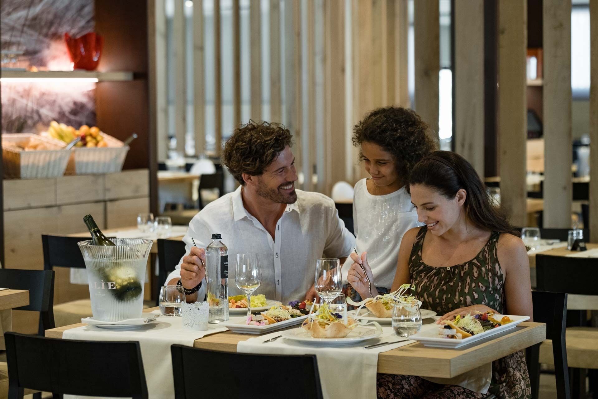 A dining area with tables set for four people, each with plates of food, glasses, and a bottle of water.
